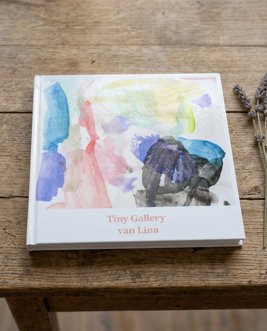 Een Tiny Gallery boek met op de cover een kleurrijke kindertekening van Lina. De speelse verfstreken zijn haarscherp gedrukt op een strakke, witte kaft, een persoonlijk en tastbaar boek waarin kinderherinneringen worden gebundeld en bewaard.