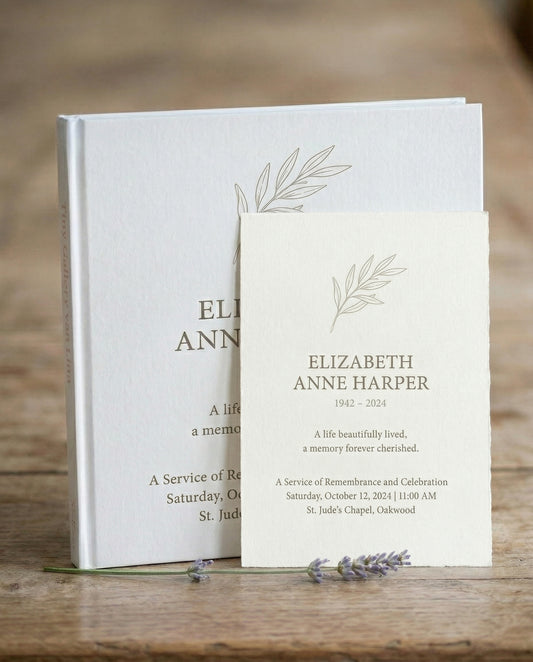 Wit Tiny Gallery kunstboek als herinneringsboek met een getekend olijftakje op de omslag, met ervoor de bijpassende rouwkaart van Elizabeth Anne Harper, op een houten tafel met lavendel