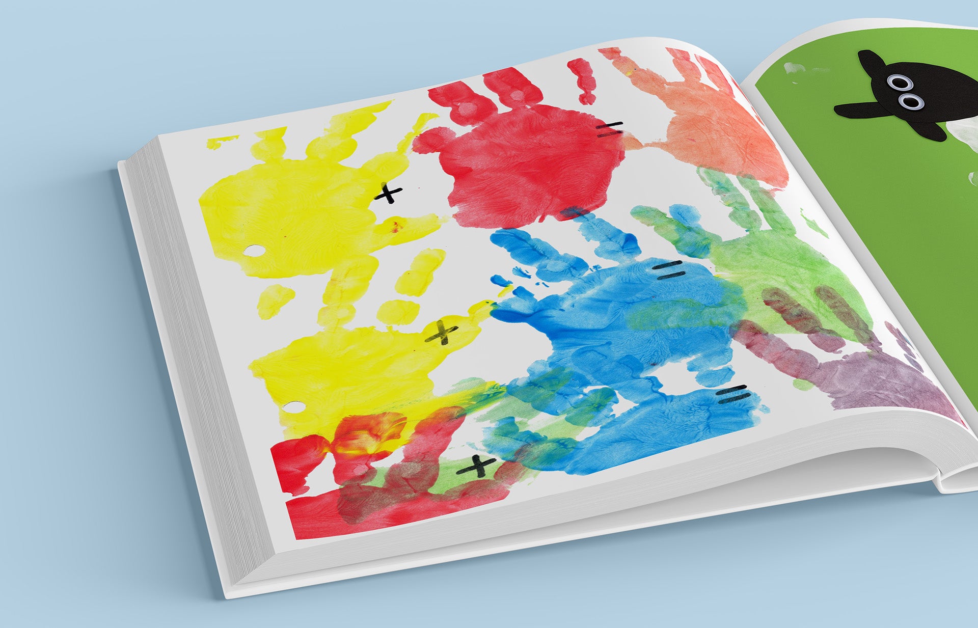 Openliggend Tiny Gallery boek met kleurrijke handafdrukken in geel, rood, blauw, groen en paars. Er staan plus- en gelijktekens tussen de afdrukken, alsof het een speelse rekenopdracht is. Rechts is deels een groene pagina zichtbaar met een zwart schaapje erop.