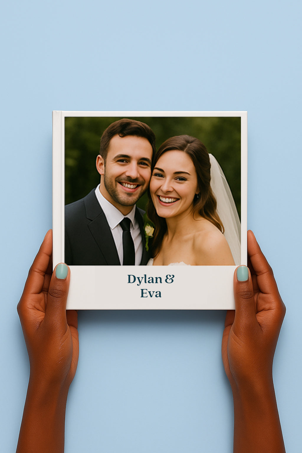 Een persoon houdt een gepersonaliseerd trouwboek vast tegen een lichtblauwe achtergrond. Op de cover staat een foto van een bruidspaar dat breed glimlacht, met daaronder de tekst “Dylan & Eva” in blauwe letters.